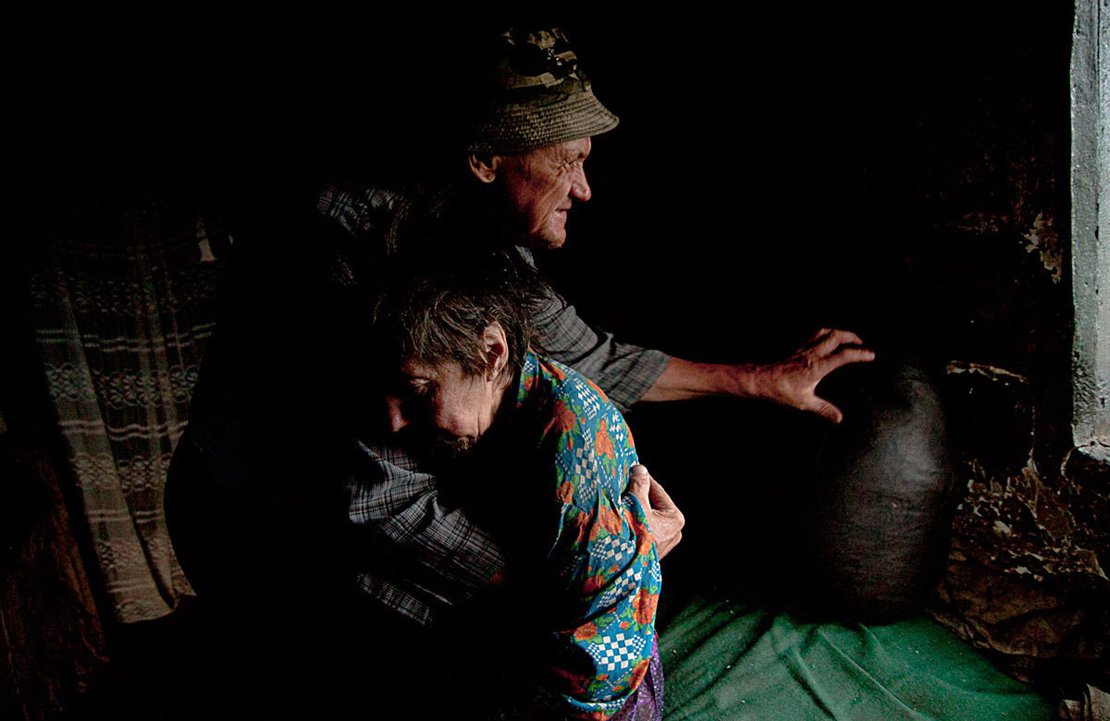 Achim, a blind man, helps his paralyzed wife, Maria, to stand so he can feed her. Sfistofca, Romania, 2012.