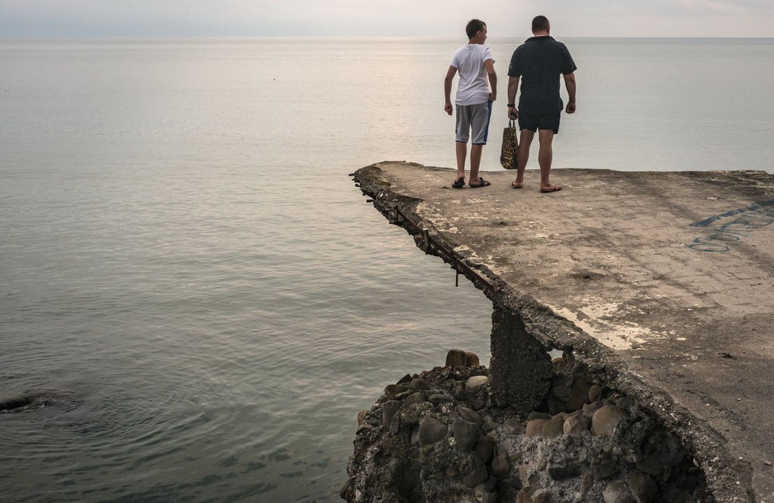 Two men are looking at the Black Sea, sitting on a concrete platform. Sukhumi