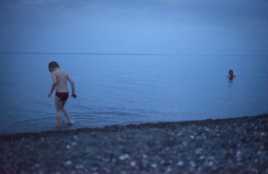 A man is smoking in the water as a kid is playing around, Sukhumi